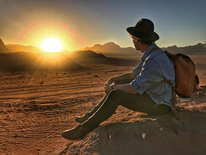 A person wearing a backpack and hat sitting on a rock watching the sun rise