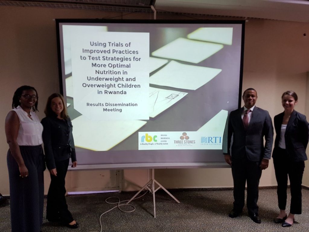 Four smiling people in business attire stand next to a projector screen