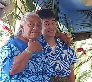 Fa’aumu’s first day with their host mother, Tuitua - posing for the camera, They are both wearing blue and white shirts and flowers show in the background