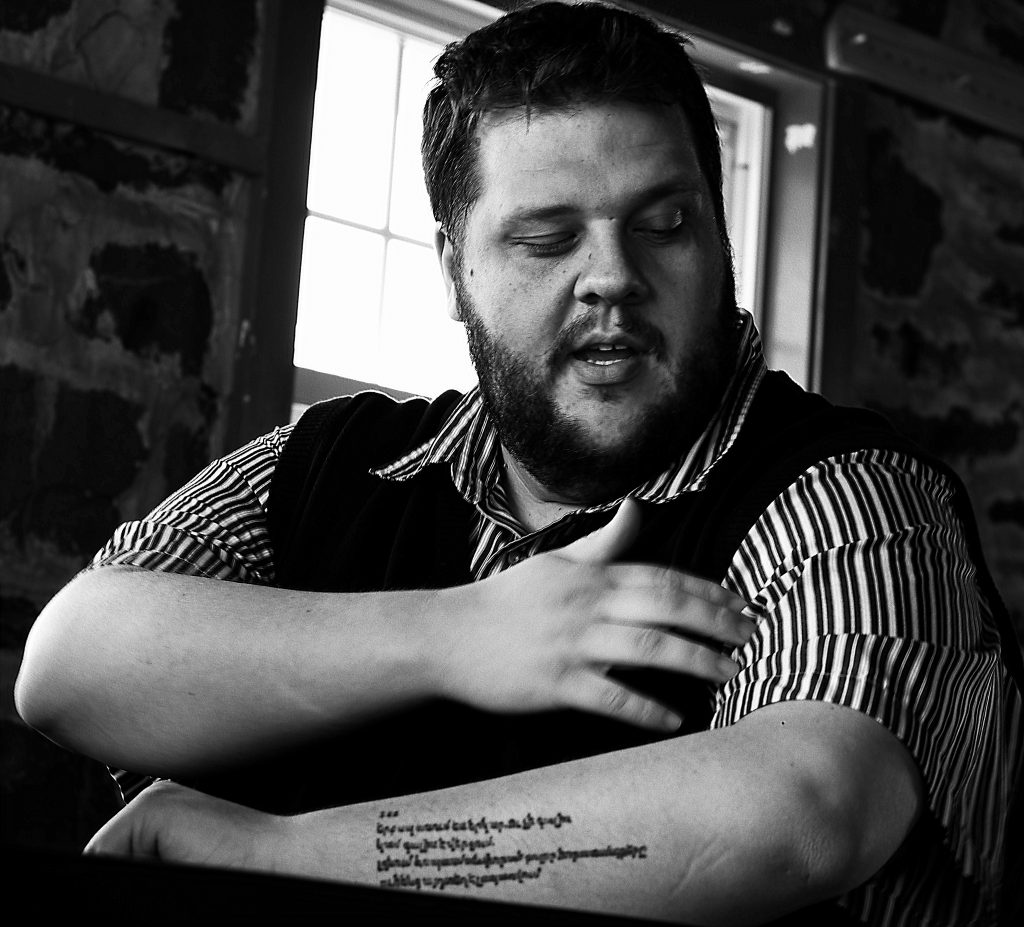 SIT alumnus and Peace Corps recruiter Adam Housh in black and white, displaying his tattooed forearm