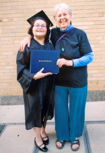 Arline Saturdayborn, a woman with short gray hair, stands next to a woman in a graduation gown. Both women are smiling.