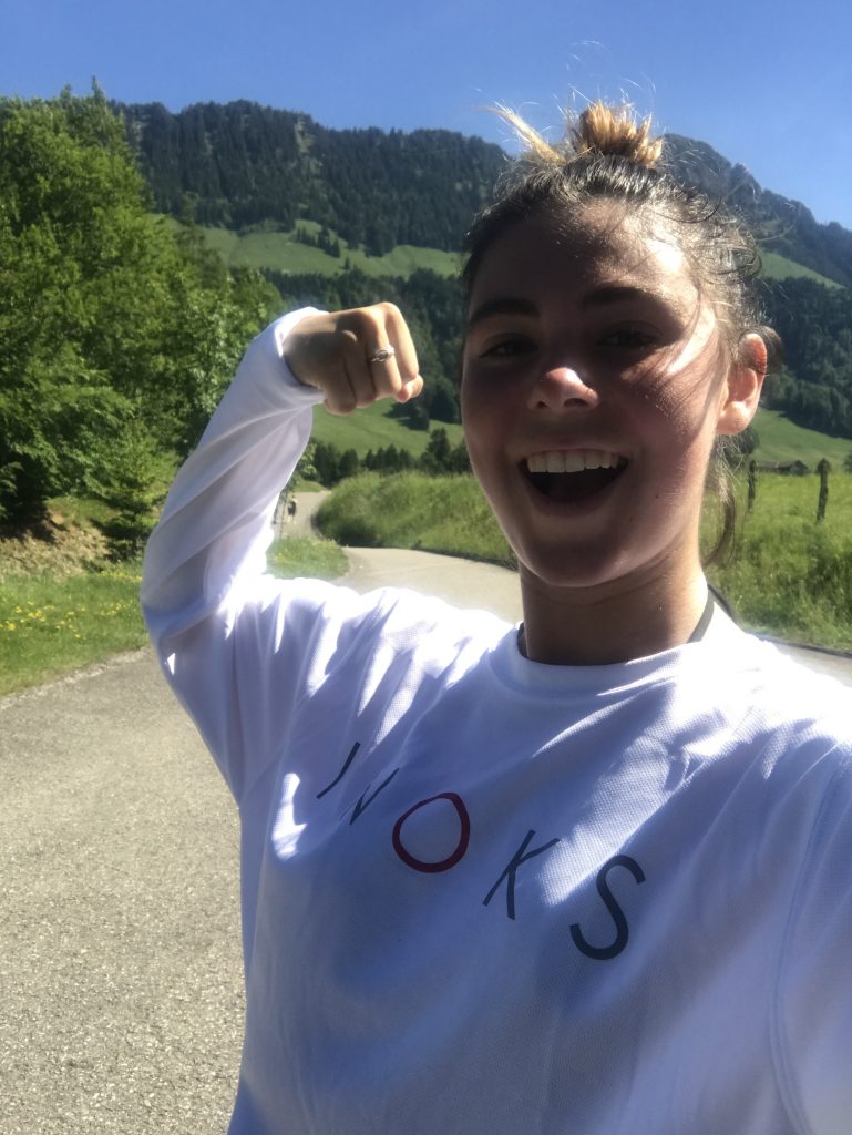 young woman smiling and showing her muscles in front of distant mountains in Switzerland