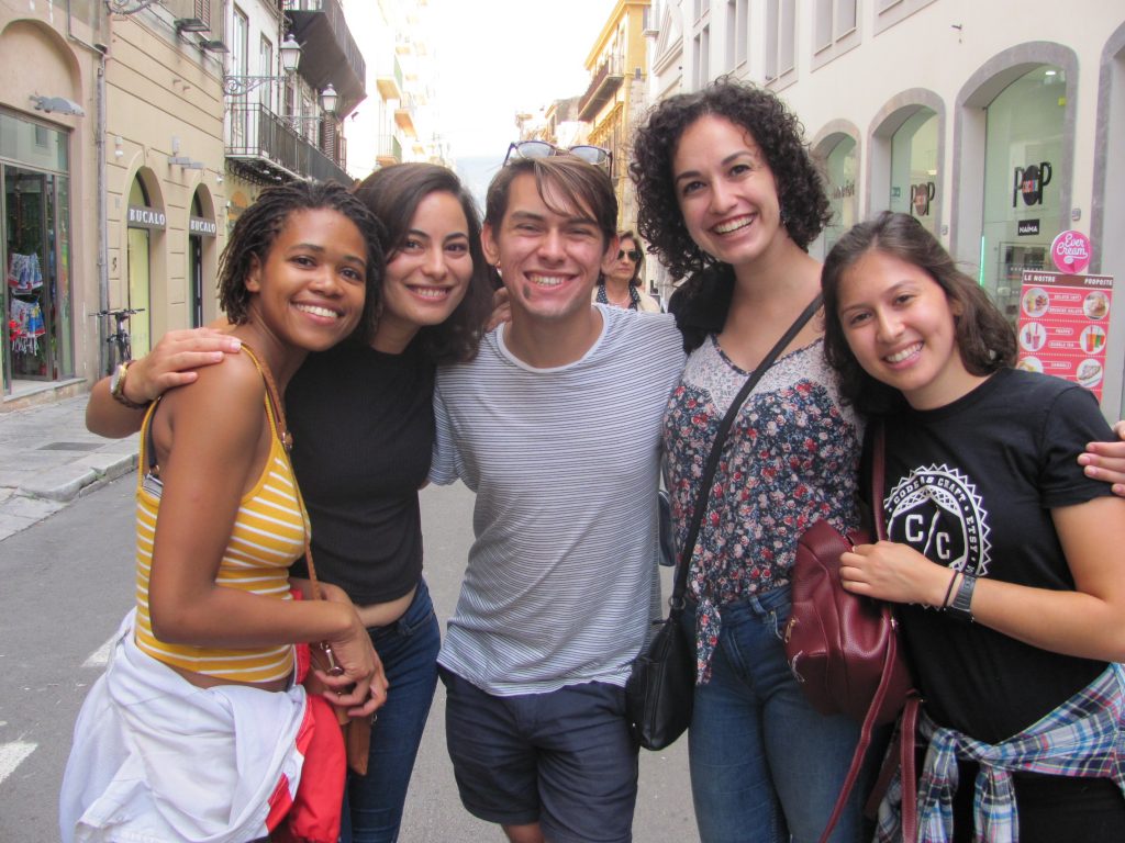 Five young people pose together and smile in a street with shops on either side