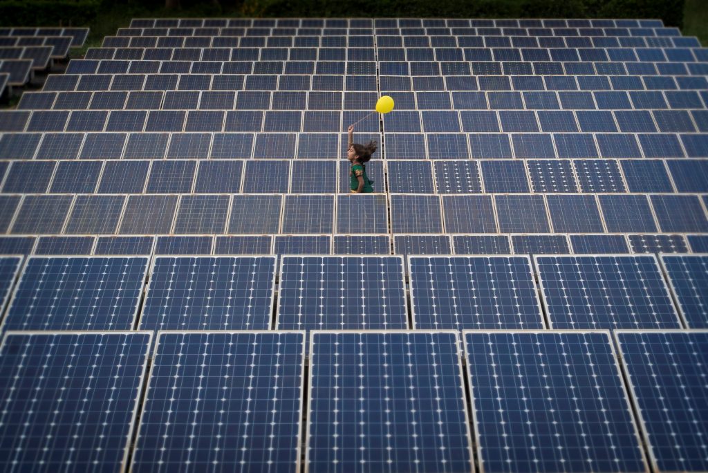 A child holding a yellow balloon runs through a field of solar panels