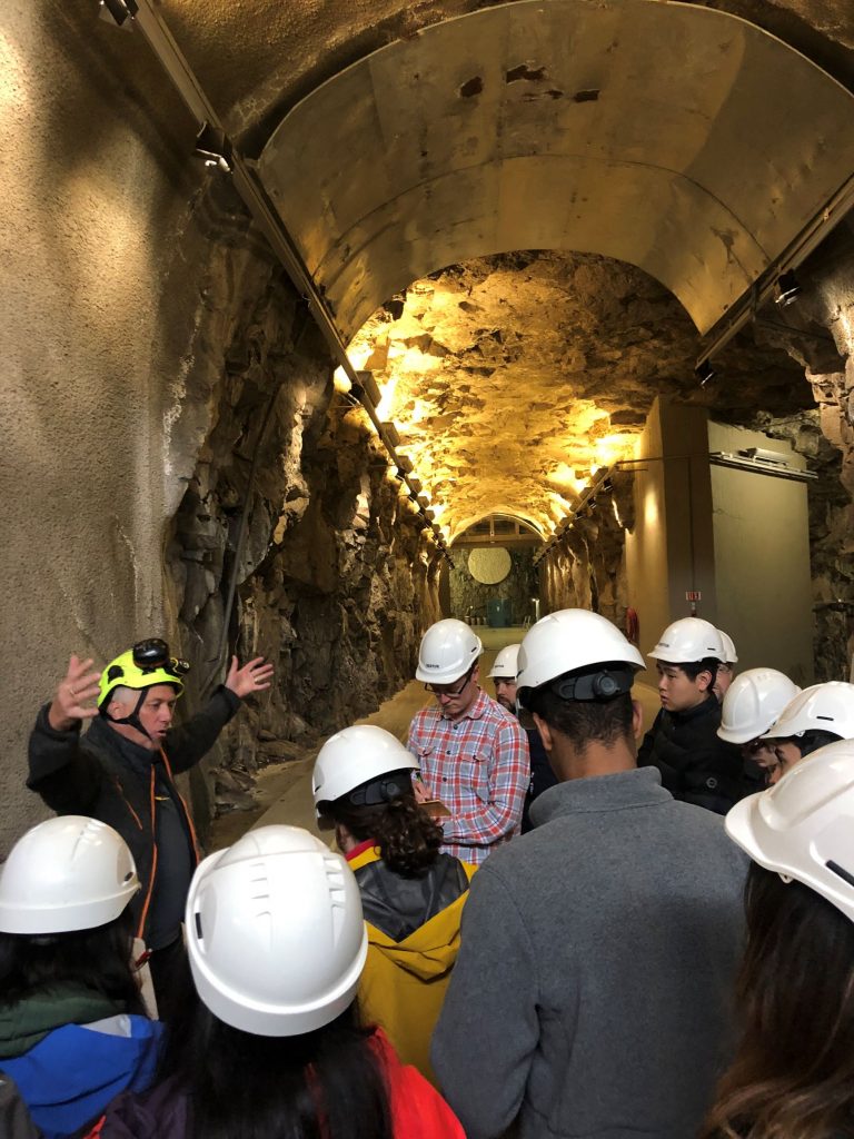 Students wearing white hardhats in  a tunnel listening to a man with arms open wide.