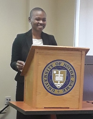 A young woman smiles at a lectern featuring the University of Notre Dame logo