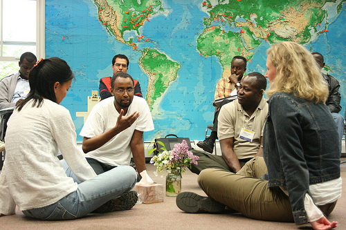 Four people sit in a circle on the floor with a world map in the background