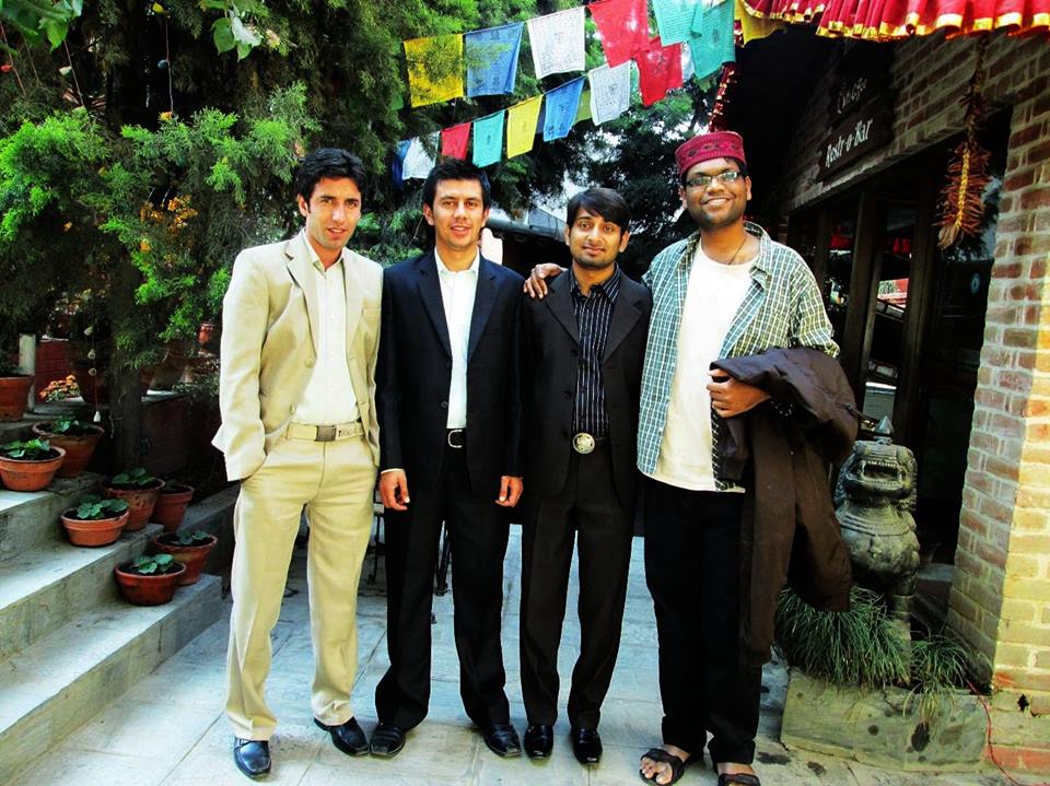 Four men face the camera, prayer flags hand overhead