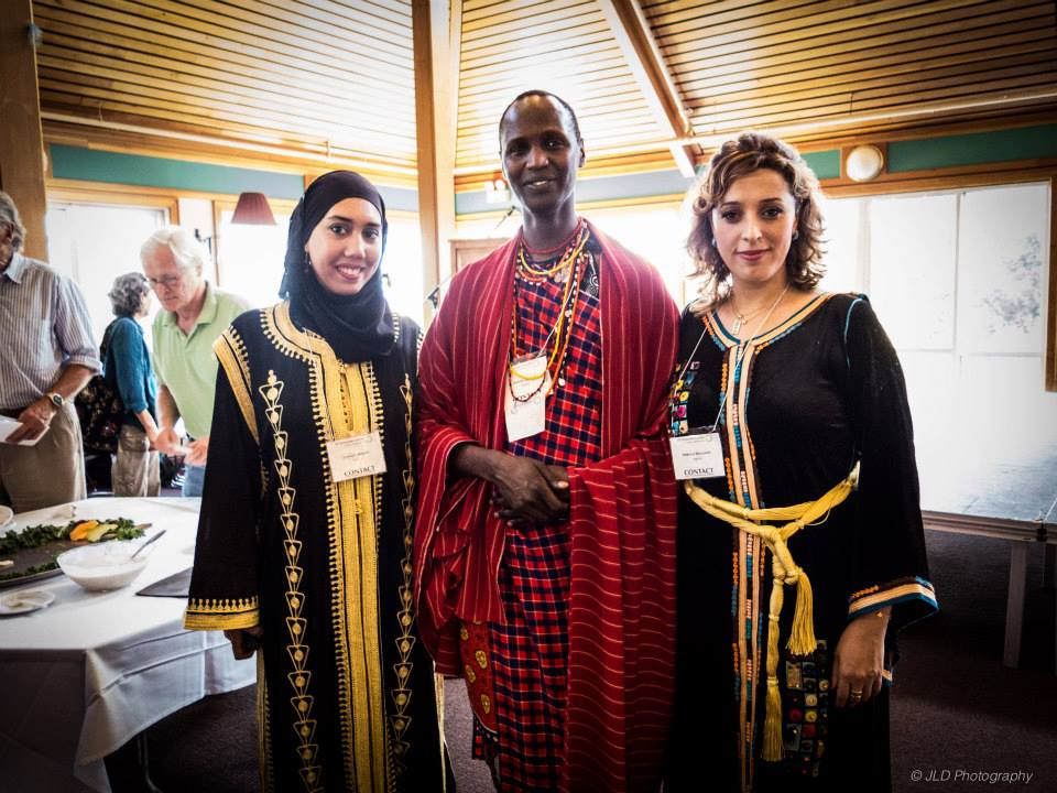 Three people face the camera wearing tunics and indigenous clothing