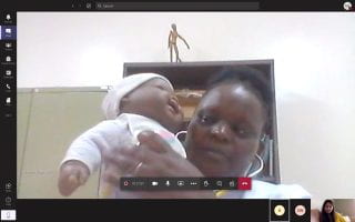 A screenshot of a woman using a baby doll to demonstrate how to perform a physical examination