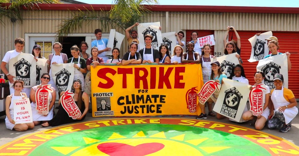 A large group of students stand with posters and a large banner that says "Strike for Climate Justice"