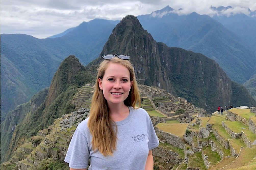 A young woman stands facing the camera with Machu Picchu in the background.