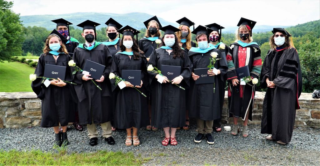 Eleven graduates in black gowns and black mortarboard caps with the SIT president in black gown and PhD cap. All are wearing protective masks.