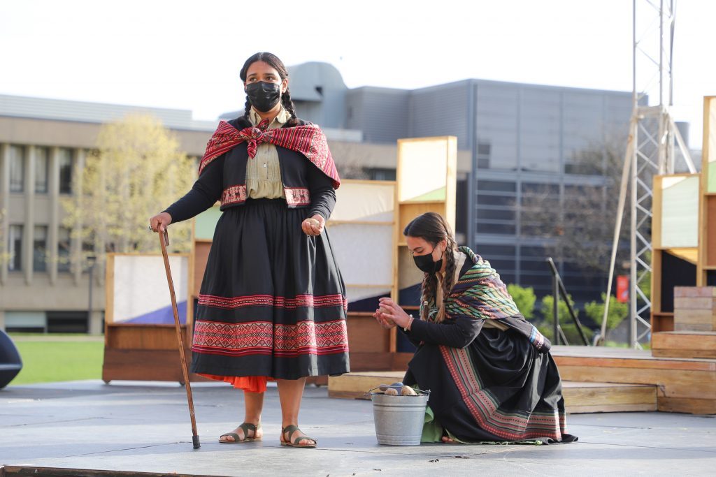 Two women in traditional Peruvian clothing perform on an outdoor stage.