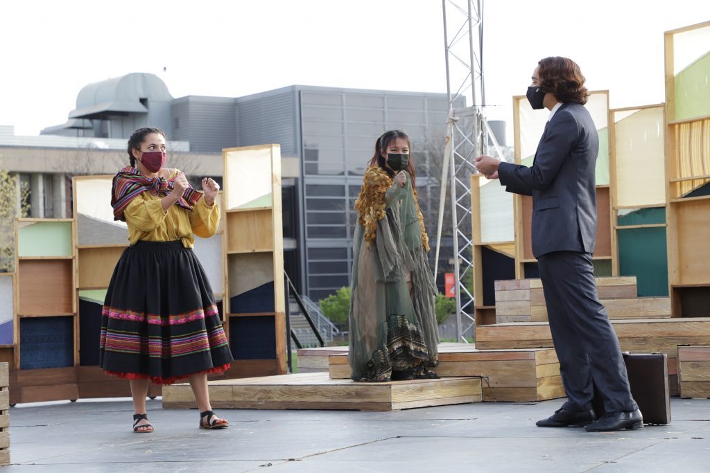 Women in traditional Peruvian clothing engage with a man in a suit on an outdoor stage as part of a play.