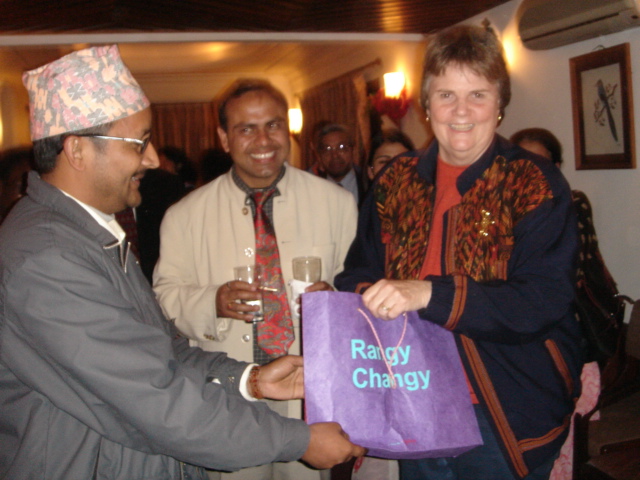 A woman smiles at the camera as a man hands her a gift bag.