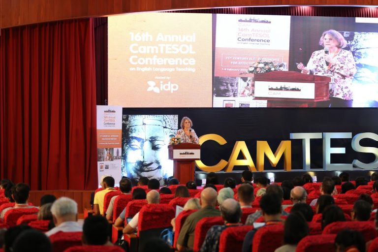 A woman speaks at a podium in a large auditorium.