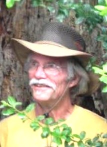 A man with a gray mustache, wearing a brimmed hat and glasses