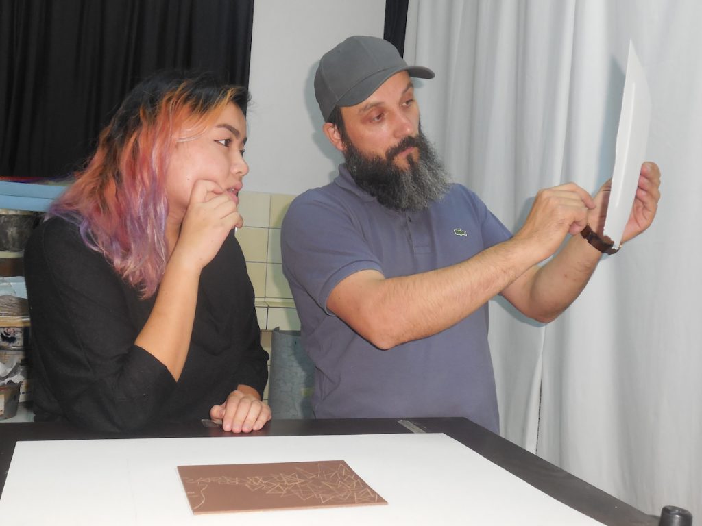 A female student gazes at a print  held by a man with a beard.