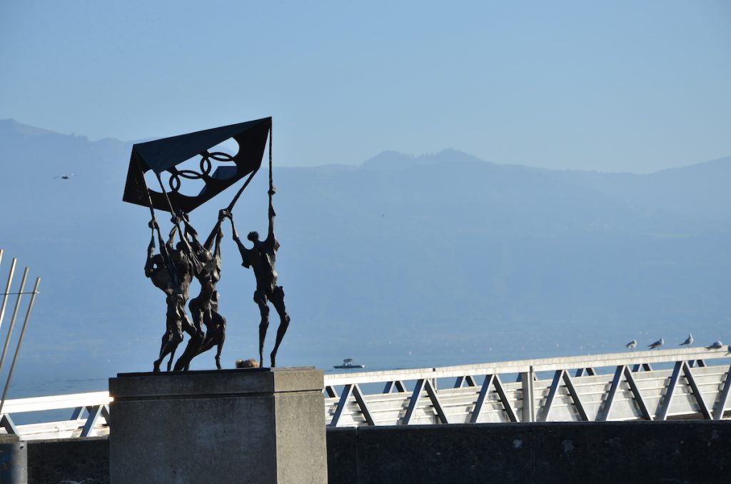 A modern metal status of tall humans holding a flag. In the background is a mountain and a bridge.