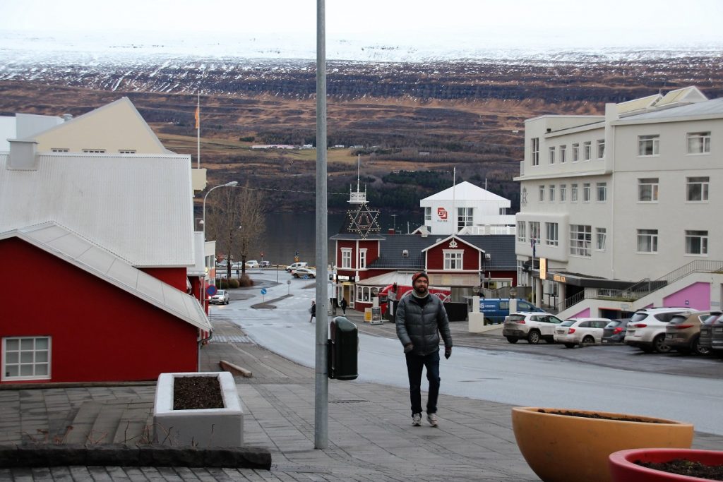 A man walking alone a street with red and white wooden buildings.