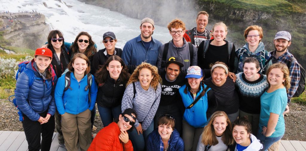 A group of about 20 young people smile for the camera. They are wearing cold-weather gear and are in a rural setting.