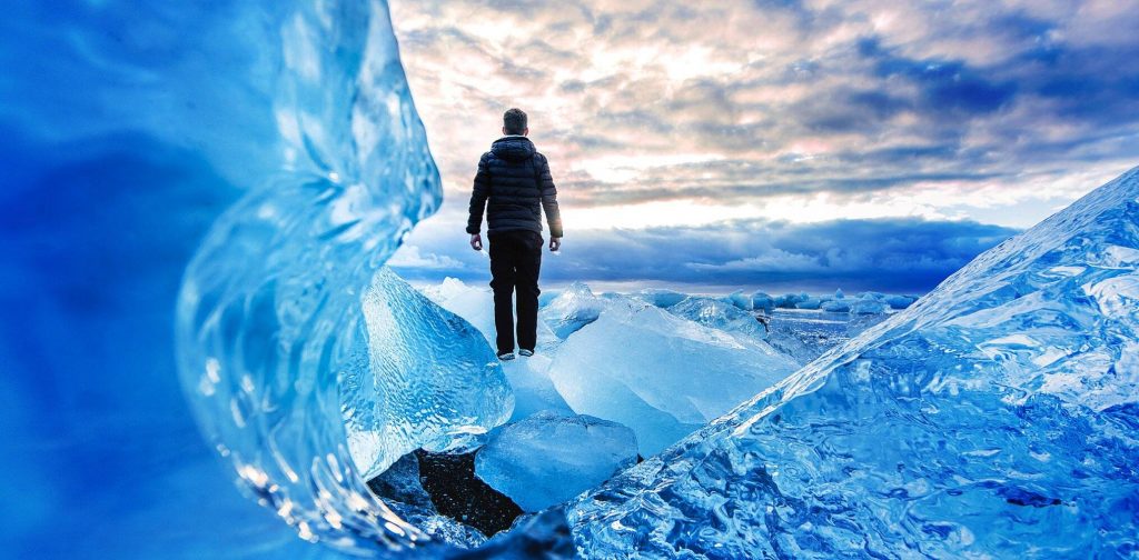 A human figure stands on an icy glacier looking toward the horizon.