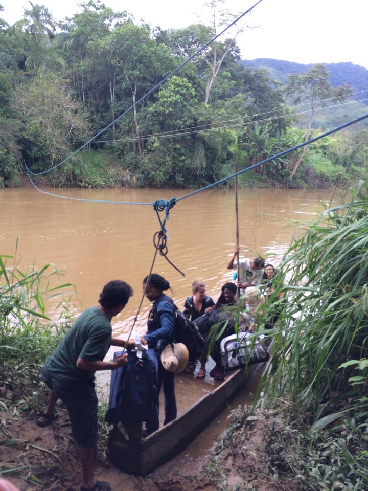 A group of young people load into a small boat, preparing to cross a muddy river