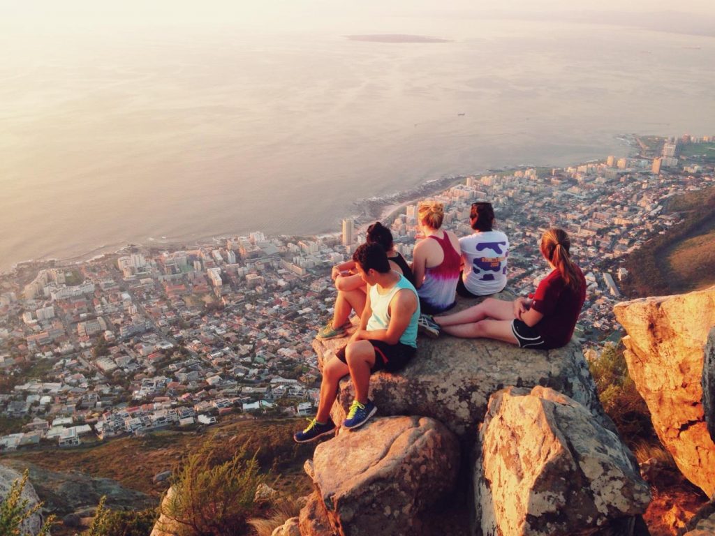 A group of young people sit on a rock overlooking the city of Cape Town.