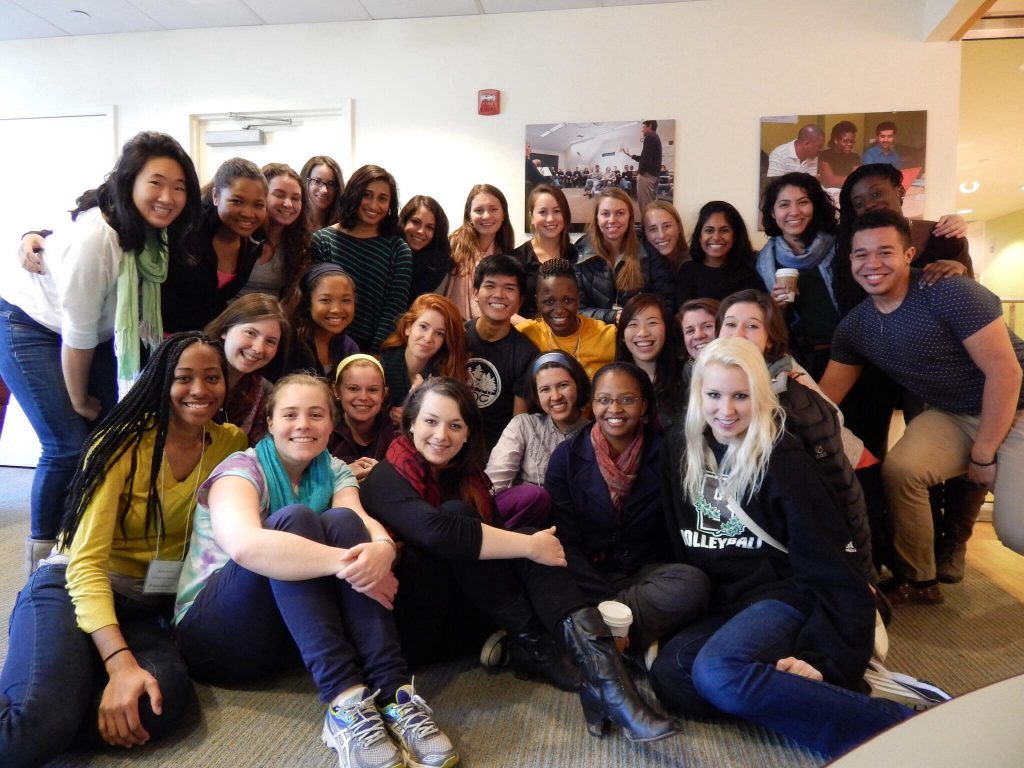 A multicultural group of approximately 30 young men and women smile for a photo.