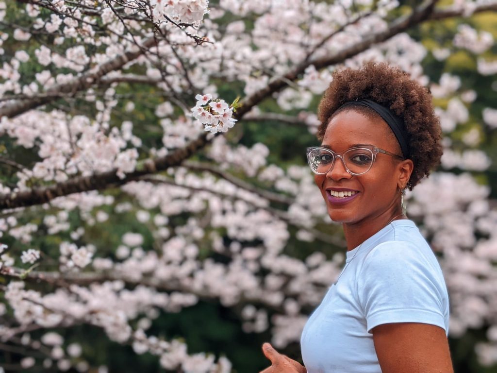 A woman with glasses stands in front of a blossoming cherry tree