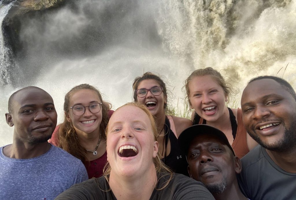 Seven people smile at the camera against a background of whitewater or a waterfall