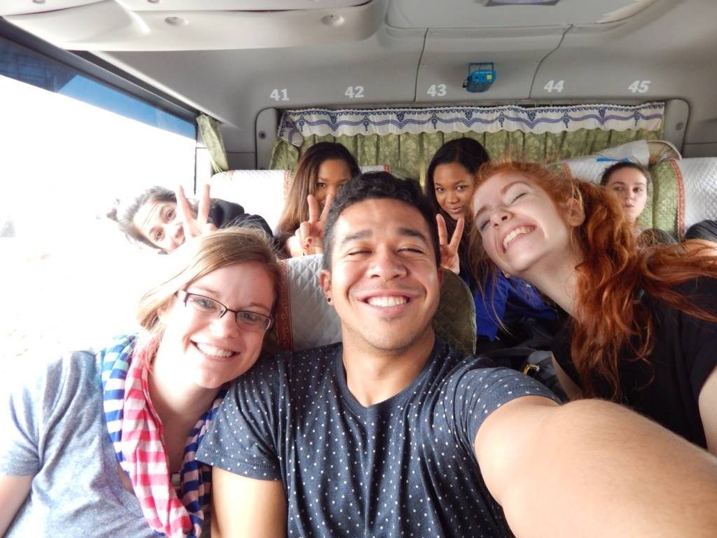 A group of young people smile and make peace signs on a bus.