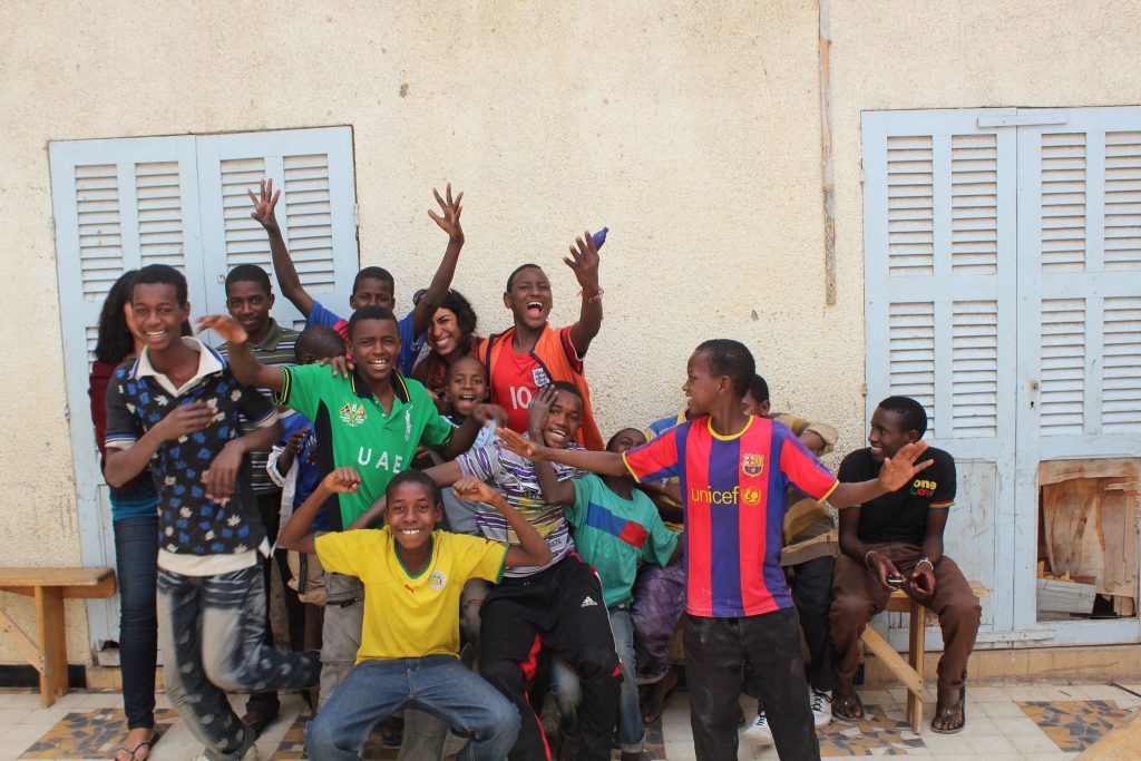 A group of young boys in Africa, many with their arms out and smiling