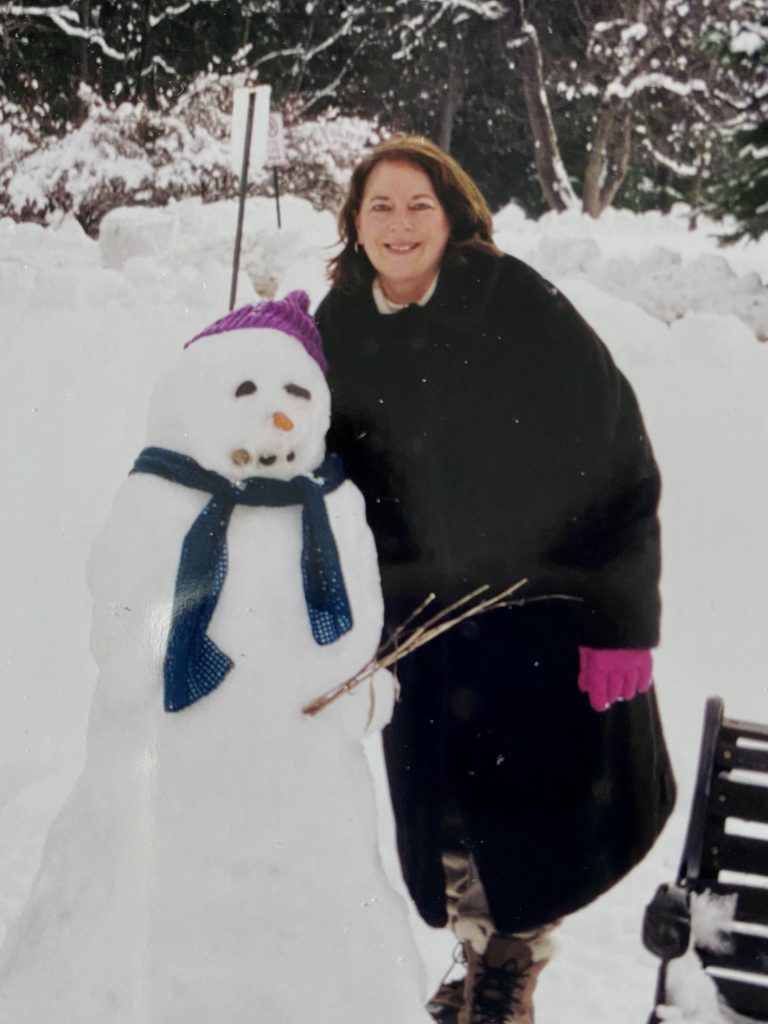 A woman with a heavy coat stands next to a snowperson
