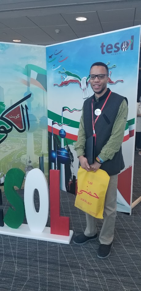 A young man stands next to a TESOL sign.