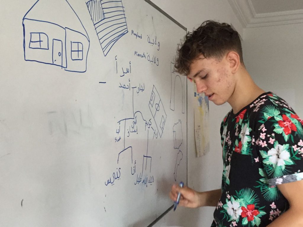 A young man draws a diagram on a white board with Arabic language labels
