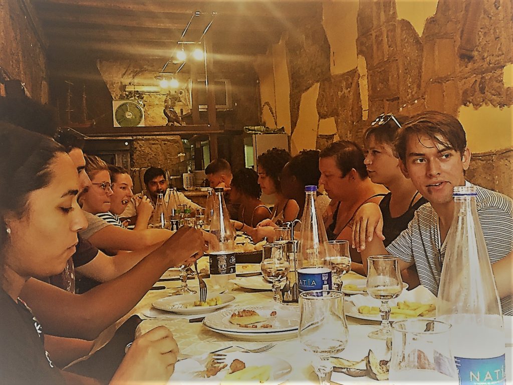 Students seated at a long table crowded with plates of food and bottles of water