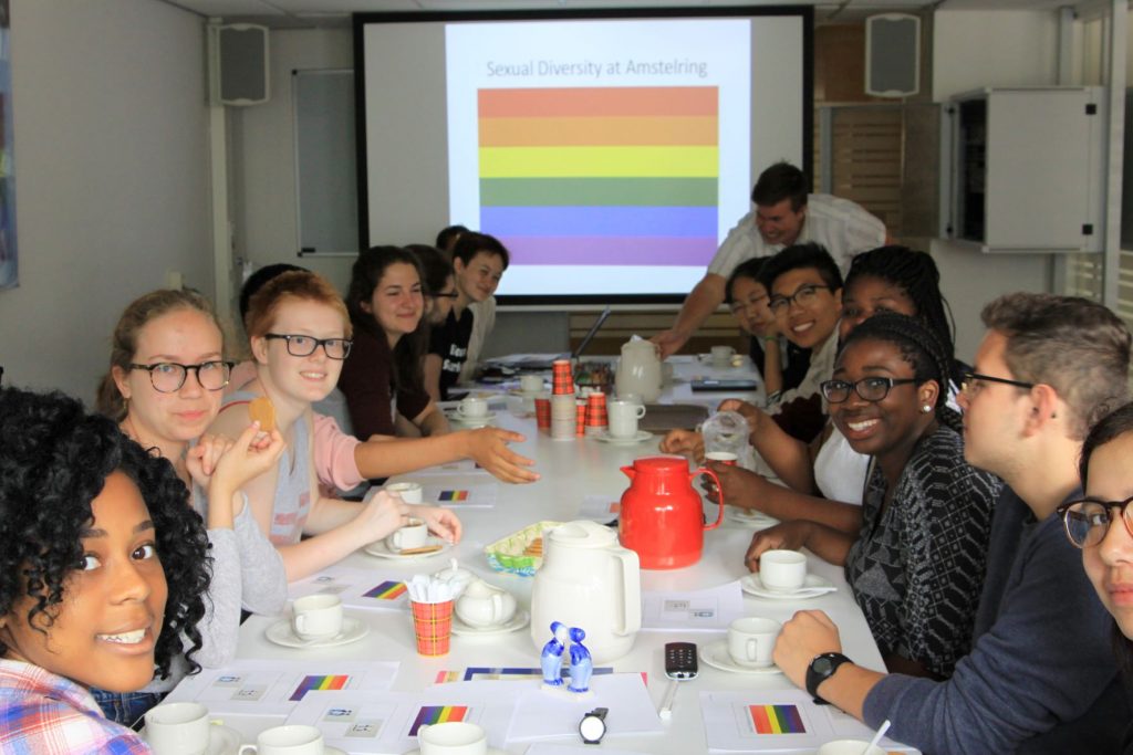 A group of students at a table; the image of a rainbow flag is on the screen in front of them