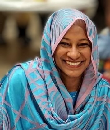A woman with a blue and pink head scarf smiles broadly.