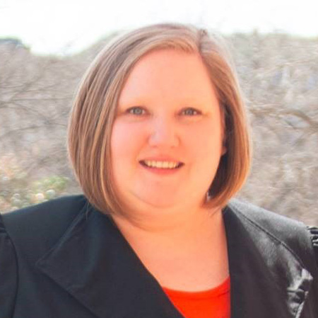 A woman with chin-length reddish blonder hair smiles toward the camera