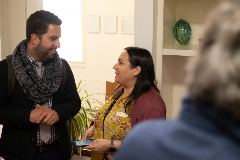 A man with a beard smiles as he chats with a woman right brown hair.