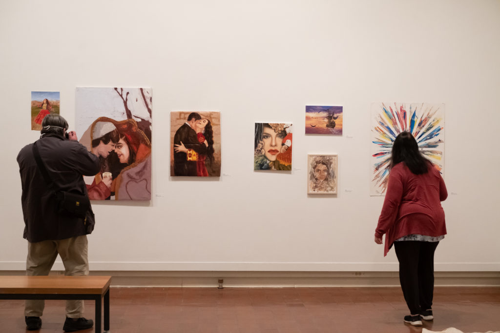 Two people look at artwork hanging on a wall,