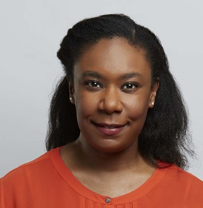 A young woman with long dark hair and small earrings wearing an orange blouse.