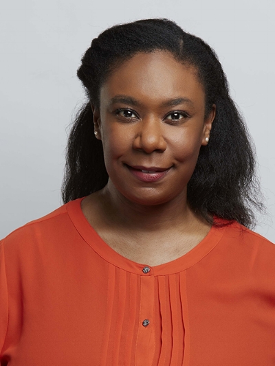 A woman with long dark hair, wearing an orange blouse, smiles at the camera.