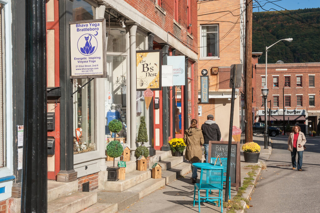 A small-town street with shops, signs, and a blue table and chairs on the sidewalk.