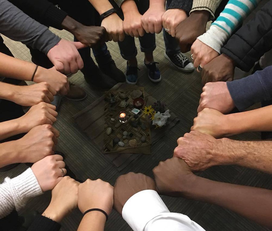 A circle of hands of different skin colors, closed with palms down.