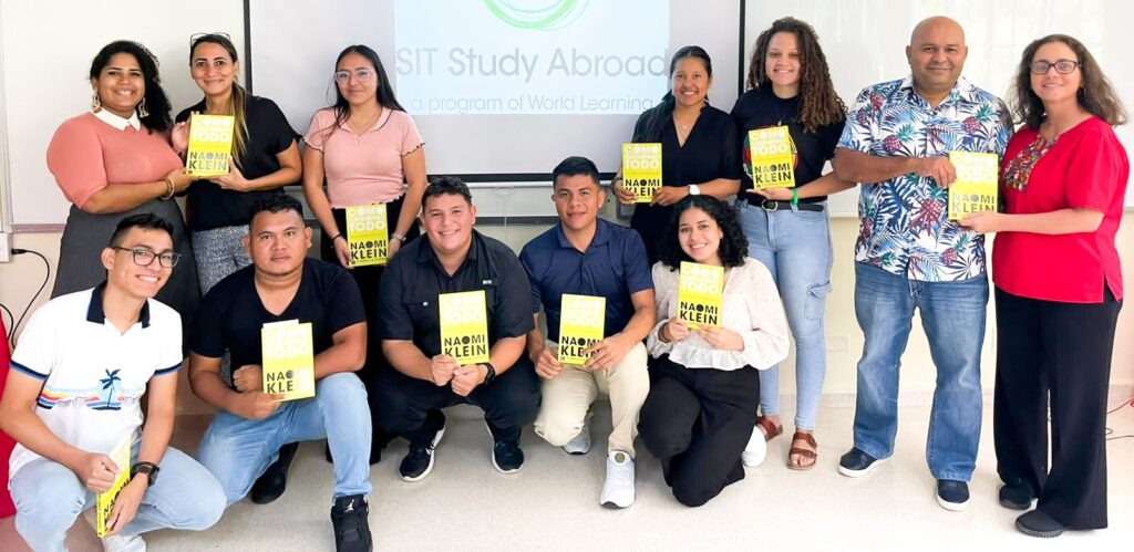 Ten students and two adults hold copies of a book by Naomi Klein.
