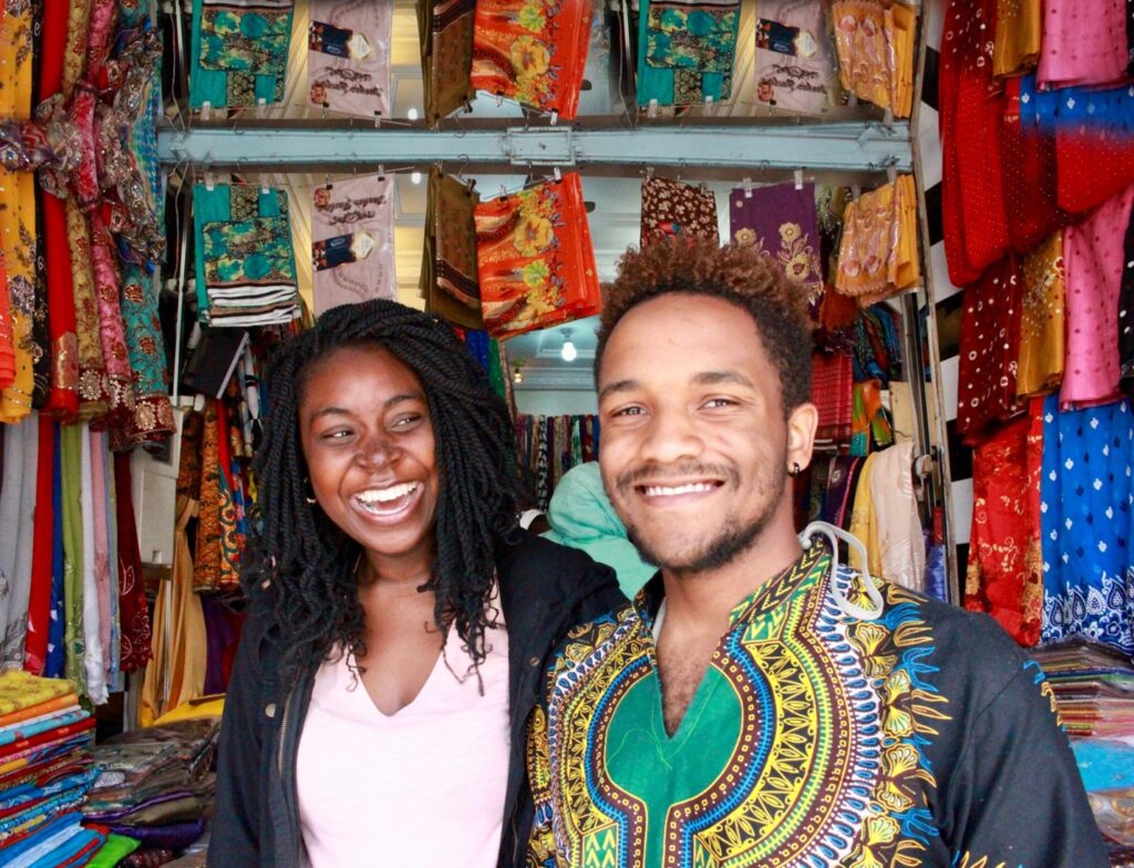 Two young students smile in a room decorated with traditional African prints.