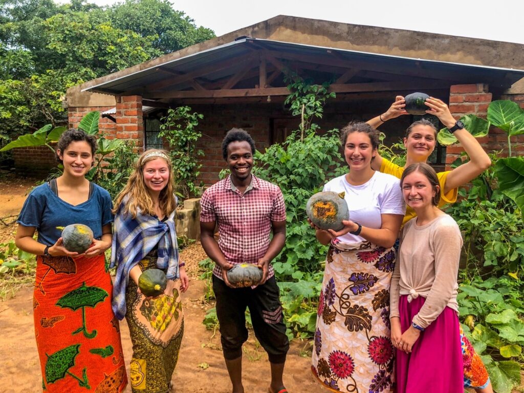 Students wearing traditional African clothing hold up produce. 